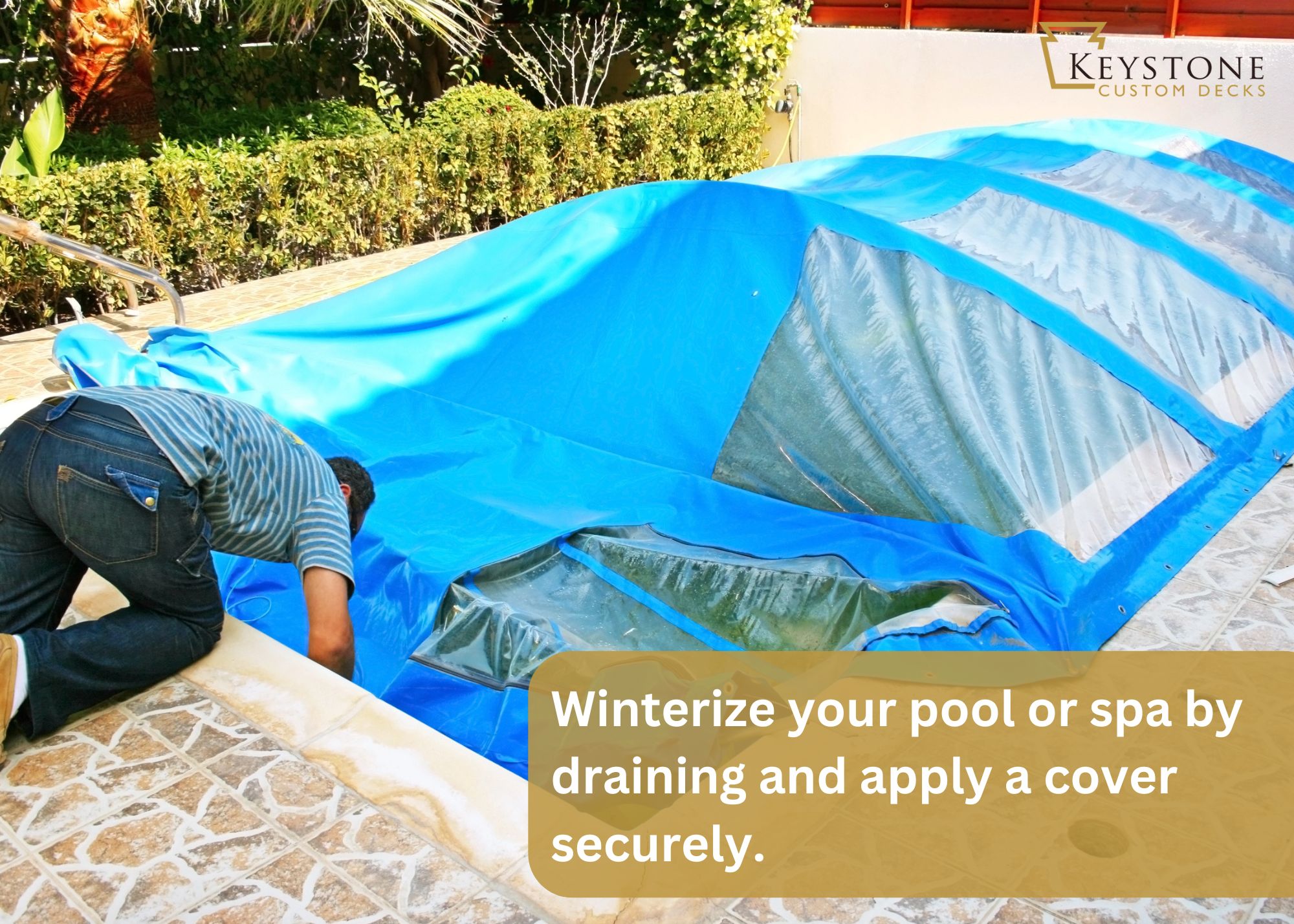 Person winterizing a pool by securing a blue cover over it. Surrounding area includes a stone patio and greenery. Text on image reads: "Winterize your pool or spa by draining and applying a cover securely.